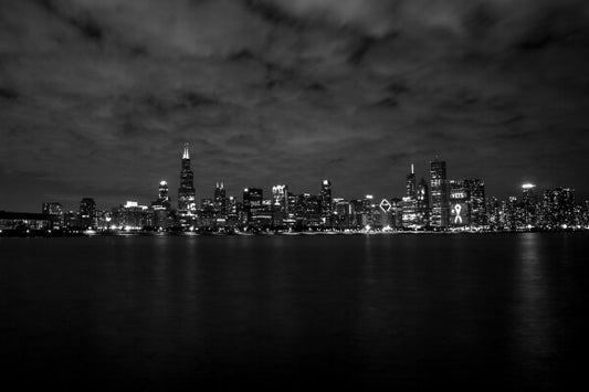 Experience the beauty and grandeur of the Windy City at night with this stunning black and white photograph of Chicago's skyline, taken from a boat on Lake Michigan. Marvel at the glittering skyscrapers and their reflections on the water, and imagine yourself gliding past on a calm summer evening.